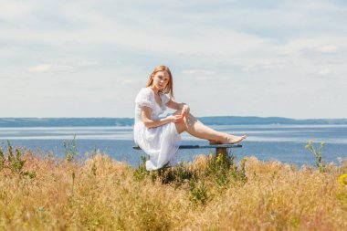 Güzel bir kız deniz kenarındaki banklarda oturuyor, gökyüzünü yakından görüyor.