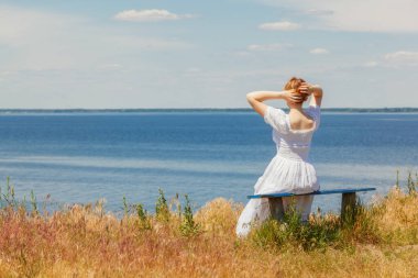 Güzel bir kız deniz kenarındaki banklarda oturuyor, gökyüzünü yakından görüyor.