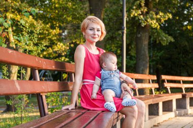 beautiful mother with her daughter and son are sitting on a bench in the park in the summer close-up