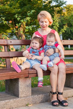 Güzel anne, kızı ve oğluyla birlikte yazın yakın planda bir bankta oturuyor.