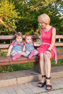 Güzel anne, kızı ve oğluyla birlikte yazın yakın planda bir bankta oturuyor.