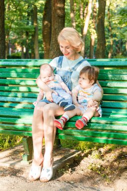 Çocuklu güzel bir kız parktaki bankta oturuyor.