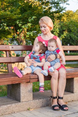 Güzel anne, kızı ve oğluyla birlikte yazın yakın planda bir bankta oturuyor.
