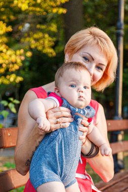 Güzel anne, kızı ve oğluyla birlikte yazın yakın planda bir bankta oturuyor.