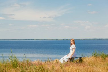 Güzel bir kız deniz kenarındaki banklarda oturuyor, gökyüzünü yakından görüyor.