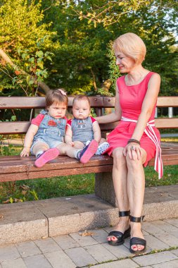 Güzel anne, kızı ve oğluyla birlikte yazın yakın planda bir bankta oturuyor.