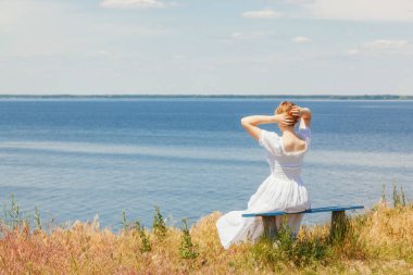 Güzel bir kız deniz kenarındaki banklarda oturuyor, gökyüzünü yakından görüyor.