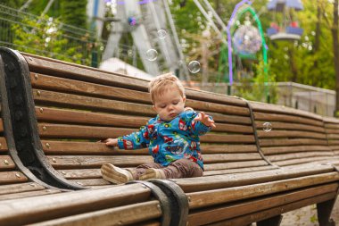 Parkta bir bankta sabun köpüğü yakalayan küçük bir çocuğun portresi.