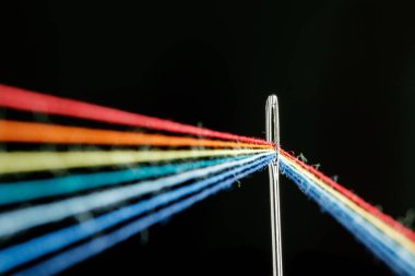 multi-colored threads for sewing in the form of a rainbow pass through an antique needle on a black background close-up