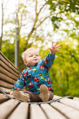 Parkta bir bankta sabun köpüğü yakalayan küçük bir çocuğun portresi.