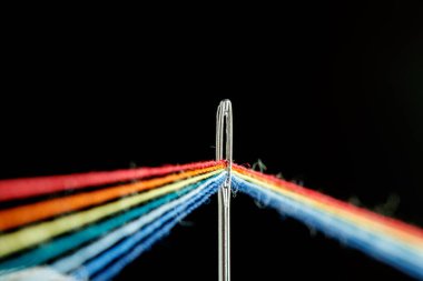multi-colored threads for sewing in the form of a rainbow pass through an antique needle on a black background close-up