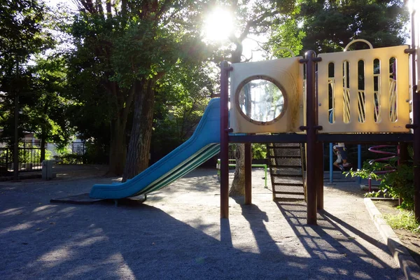 A playground in a nice park with a slide playground where the sun shines through the trees