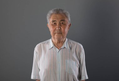 Gri arka planda yaşlı bir Asyalının portresi.