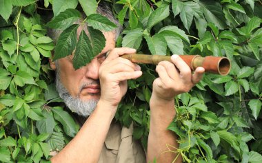 Elinde dürbünlü bir adam yaprakların arasında saklanıyor.