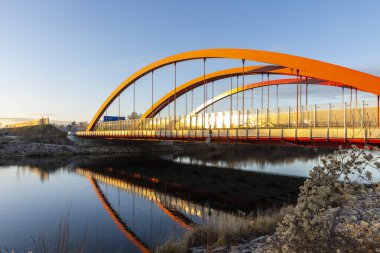 Augsburg yakınlarındaki Lech nehri üzerindeki karayolu köprüsünün kıvrımlı kırmızı kemerleri akşam güneşinin ışığında