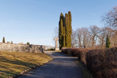 Bavyera 'daki Wessobrunn mezarlığındaki çakıl yolu iki yaşam ağacının ve mavi gökyüzünün manzarasının yanındaki geçide çıkar.
