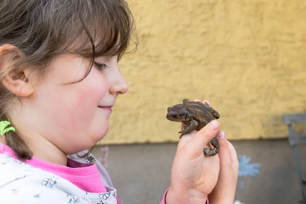 Küçük bir kız elinde bir kurbağa olmasından mutlu.