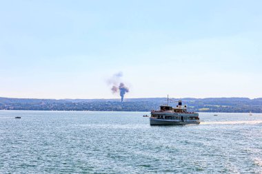 Germany, Herrsching 08-23-2022, view over the Ammersee in direction Dieen with the ferryboat Utting in the foreground and the smoke plume of a building fire.