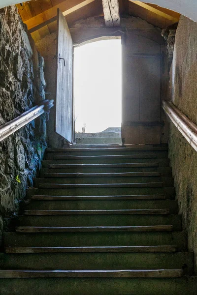 Staircase in an old masonry to a half-opened door into the light At the Loreto Chapel in Bhl am Alpsee near Immenstadt.