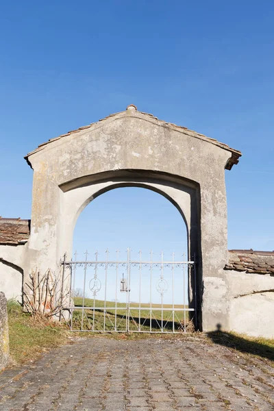 Old gate with wrought iron door grille at cemetery in Wassobrunn in Bavaria overlooking blue sky and meadow