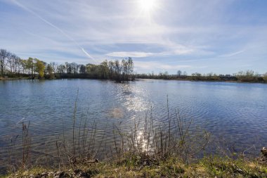 Güneş küçük bir gölün su yüzeyinde mavi gökyüzüne küçük yıldızlar şeklinde yansıyor.