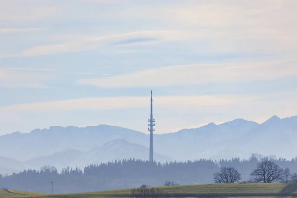 Transmission tower near Hohenpeissenberg in Bavaria against a slightly blurred backdrop of the Ammergau Alps in pastel colors