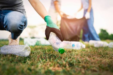 Kadın eli parkta temizlik için plastik şişe topluyor.