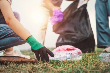 Kadın eli parkta temizlik için plastik şişe topluyor.