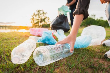 Kadın eli parkta temizlik için plastik şişe topluyor.