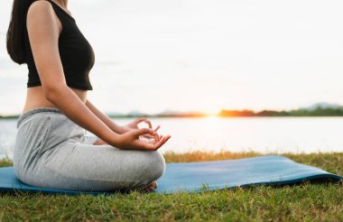 Kadın Yoga nehir doğası yakınında oturuyor.