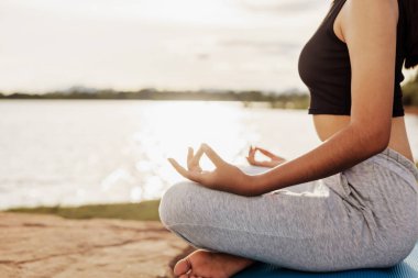 Kadın Yoga nehir doğası yakınında oturuyor.