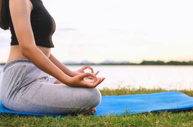 Kadın Yoga nehir doğası yakınında oturuyor.