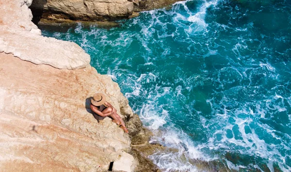 Schöne Mädchen sitzt auf einem hohen Felsen und blickt auf das Meer. Ansicht von oben. — Stockfoto