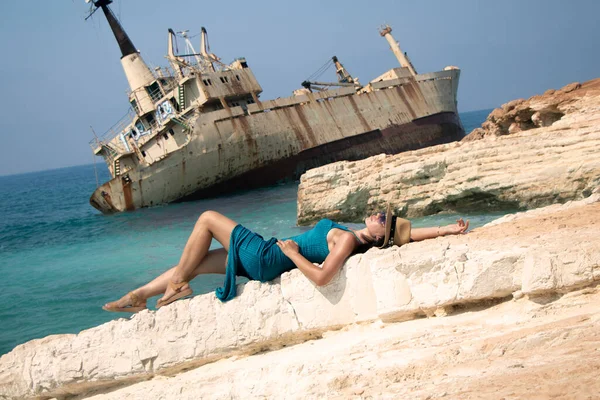 Молодая женщина лежит на скале на фоне заброшенного корабля Edro III — стоковое фото