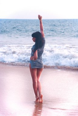 Kumsalda elini kaldırarak yürüyen genç bir kız. Tatilde. Güneşli sahil.