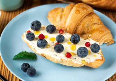 Klasik Amerikan kahvaltısı. Taze böğürtlenli Fransız kruvasanı. Krem peynirli yaban mersini ve çilek. Kruvasan ve tahta zemin üzerinde yazılı kahve olan bir fincan. Sağlıklı kahvaltı.