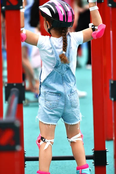 Little girl child in protective clothing helmet knee pads elbow pads with rollers. girl 6 years old on the playground. crossfit for kids. Active girl goes in for traumatic sports.