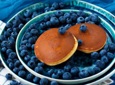 selective focus. pancakes with blueberries on a blue plate. Lots of fresh blueberries scattered around. Delicious dessert with berries for breakfast. High quality photo