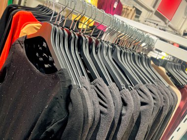 clothes on a rack in a store. Wardrobe with same black dresses and t-shirts. black womens Fashion clothes hanging on hangers. Closeup on group of accessory, household showroom department