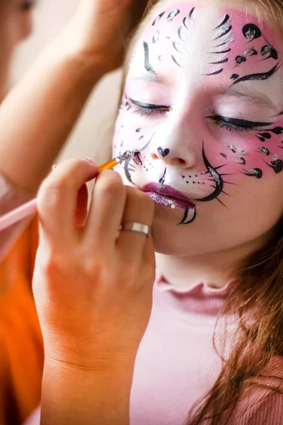 Cute makeup little tiger. face painting outdoors, having fun, copy space. girl with aqua makeup of tiger muzzle. Master making aqua makeup on girl face. aqua grimm on birthday or halloween party