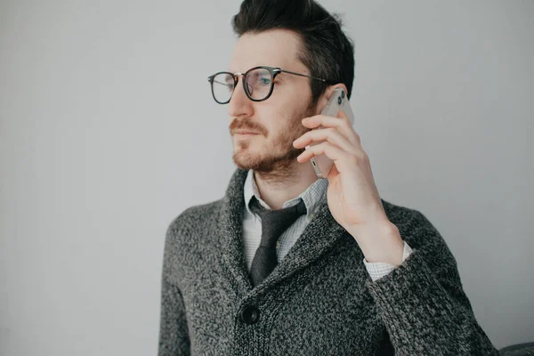 Молодий стильний чоловік з бородою і окулярами в сорочці і сірий кардиган на сірій стіні кличе — стокове фото