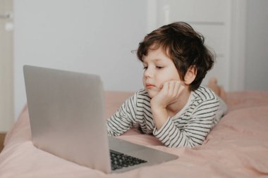 Küçük çocuk yatak odasında yatar ve dizüstü bilgisayara bakar.