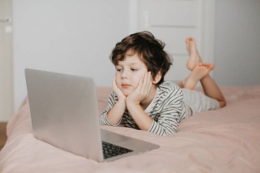 Küçük çocuk yatak odasında yatar ve dizüstü bilgisayara bakar.