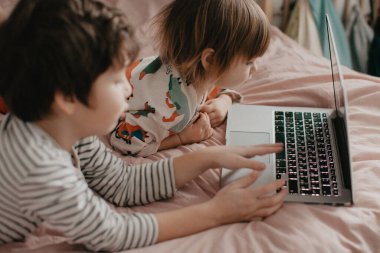 Küçük erkek ve kız kardeş yatak odasında yatar ve dizüstü bilgisayara bakar. Yüksek kalite fotoğraf