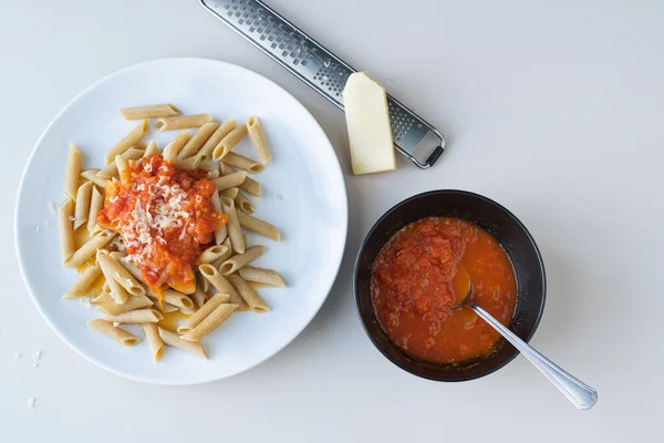 Pasta plate with tomato on white background. Piece of cheese and grater. Bowl with tomato. Copy space. Top view.