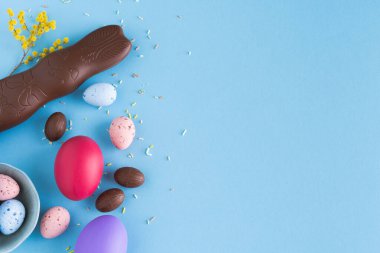 Sarı çiçekli mavi arka planda Paskalya yumurtası ve çikolatalı tavşan. Üst Manzara. Boşluğu kopyala.