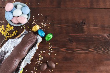Koyu ahşap arka planda, sarı çiçekli Paskalya yumurtası ve çikolatalı tavşan. Üst Manzara. Boşluğu kopyala.
