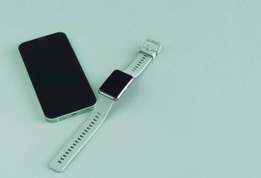 Yeşil arkaplanda yeşil akıllı saat ve telefon var. Uzayı kopyala Üst görünüm.