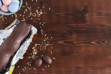 Koyu ahşap arka planda, sarı çiçekli Paskalya yumurtası ve çikolatalı tavşan. Üst Manzara. Boşluğu kopyala.