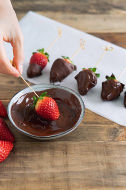 Ahşap arka planda çikolatalı çilekler. Çileği çikolata kasesine daldırmak. Uzayı kopyala Dikey fotoğraf.